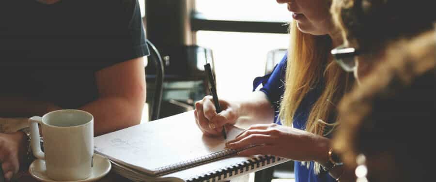 A group of people sit around a girl writing in a notebook