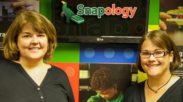 The two snapology founders stand in front of a tv screen with the snapology logo