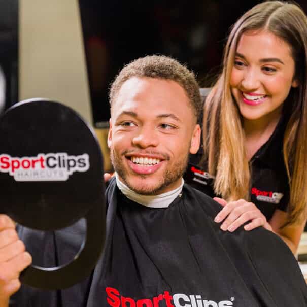 a man smiles while looking into a mirror at a sport clips