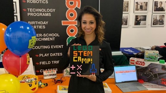 Jessica holds a handmade sign saying "Lego STEM Camp"