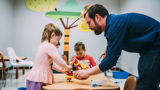 Aaron helps children build something out of legos on a table