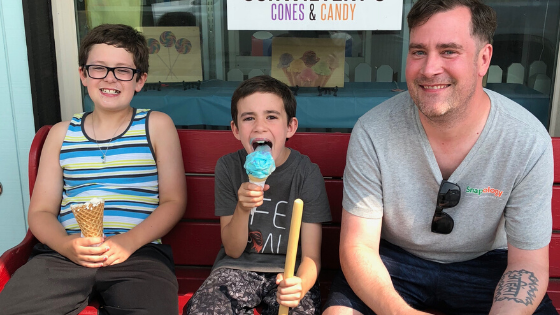 Aaron sits on a bench with his two children eating ice cream cones