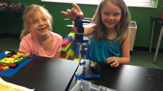 two girls play with a lego device they built